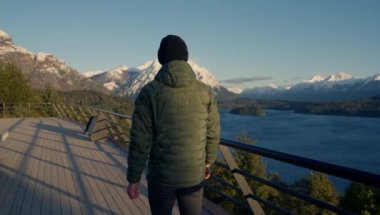 A video showing the back view of a man walking at the observation deck, sightseeing the landscape of Nahuel Huapi park at Bariloche, Argentina during daytime