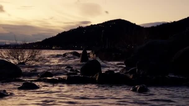 在日出的时候 在阿根廷巴里洛切的一个湖面上 一帧静止不动的山的轮廓和泼洒在岩石上的水 — 图库视频影像