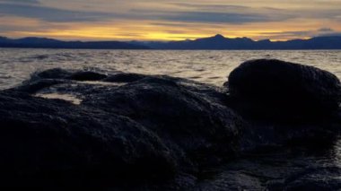 Güneş doğarken Arjantin 'in Bariloche kentindeki büyük bir göl kıyısında dalgaların su sıçrattığı ve aktığı yakın çekim.