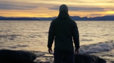Ufukta gün doğumuna karşı dalgaları seyreden ve sonra Arjantin, Bariloche 'de yürüyen bir adamın arka görüntüsü.