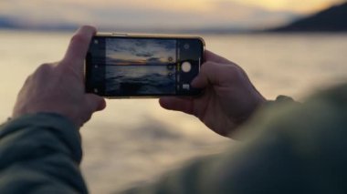Arjantin, Bariloche 'de gün doğumunda dalgaların fotoğraflarını çeken bir adamın ellerini gösteren cep telefonu görüntüsü.