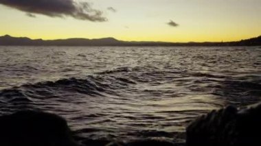 A still shot of the silhouette of rocks and mountain range, with waves flowing across the lake in Bariloche, Argentina during sunrise
