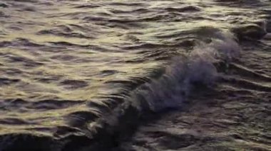 Güneş doğarken Arjantin 'in Bariloche kentindeki bir göl üzerinde yosunlu bir kayayla akan dalgaların yakın plan çekimi.