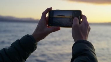 Arjantin, Bariloche 'de gün doğumunda gölün fotoğraflarını çeken bir adamın ellerini gösteren cep telefonu görüntüsü.