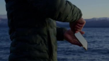 A video showing a man getting his phone from his back pocket and uses camera to capture the view at Bariloche, Argentina during sunrise