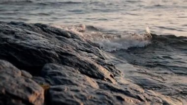 Güneş doğarken Arjantin 'in Bariloche kentindeki bir gölde kayaların yakınından geçen dalgaların yakın plan çekimi.