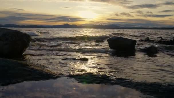 岩や山脈のシルエットの静止画で 日の出の間アルゼンチンのバリローチェの湖畔に水が流れています — ストック動画