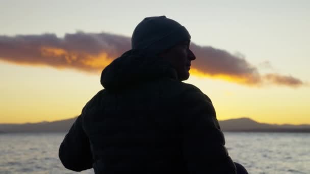 一段录像显示了一个男人坐在那里 左右张望的背影 接着在阿根廷巴里洛切的一个湖边观看日出 — 图库视频影像