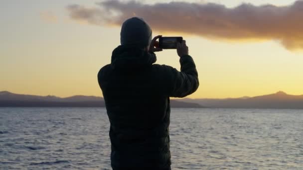 아르헨티나의 로체에 호숫가에서 핸드폰을 사용하여 아름다운 일출을 포착하고 남자의 뒷모습을 — 비디오