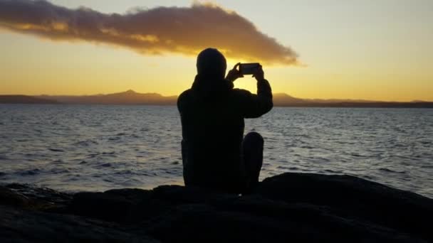 아르헨티나의 로체에 호숫가에서 핸드폰을 사용하여 아름다운 일출을 포착하고 남자가 모습을 — 비디오