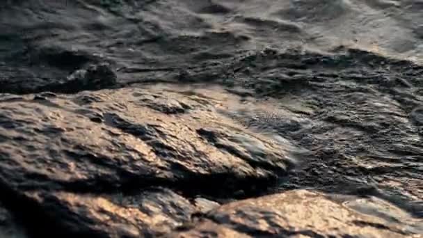 日の出の間 アルゼンチンのバリローチェの湖畔の大きな岩の上を 波が飛び散り 流れるのを間近に撮影しました — ストック動画