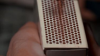 A close-up shot of a male hand holding a matchbox while the other hands lights a matchstick in slow motion