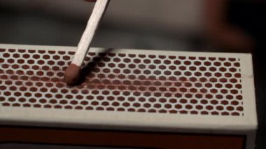 A close-up shot of a match being lit through friction with the striking surface of a matchbox