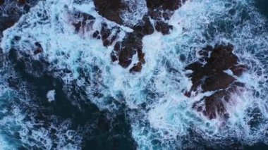 Drone over the blue sea waves crashing and flowing onto the large rocks at Benijo beach in Tenerife, Spain during daytime