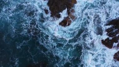 Drone flight over and descending slowly on blue sea waves and large rocks at Benijo beach in Tenerife, Spain during daytime