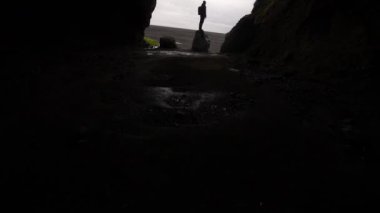 Tilt shot moving upwards revealing a man standing on a rock at the entrance of Gigjagja cave, also known as the Yoda cave in Iceland, during daytime