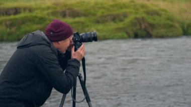 Tilt shot moving downwards showing a man using his camera mounted on a tripod on Skoga river during daytime in Iceland