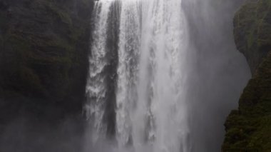 A tilt shot moving upwards showing the Skogafoss waterfall and mossy canyon located in Iceland during daytime