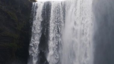 A tilt shot moving downwards showing the Skogafoss waterfall and mossy canyon located in Iceland during daytime