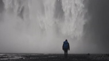A still shot of a man slowly walking towards Skogafoss waterfall located in Iceland during daytime