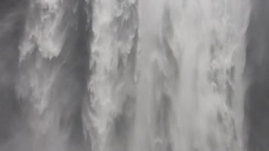 A tilt shot moving downwards showing a man standing near the Skogafoss waterfall in Iceland during daytime