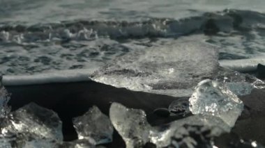 Close-up shot of sea wave crashing on ice on the black sand of Diamond Beach