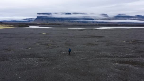 昼間アイスランドにあるジョクルサロンの溶岩の地形を歩く男のドローンショット — ストック動画