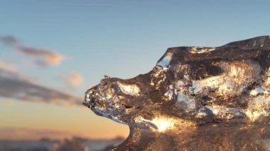 Tilting view of an iceberg's surface glistening from the sun's reflection under a blue and cloudy sky