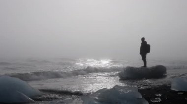 Waves with sunset reflection near a man on top of an iceberg on the coast of Diamond Beach