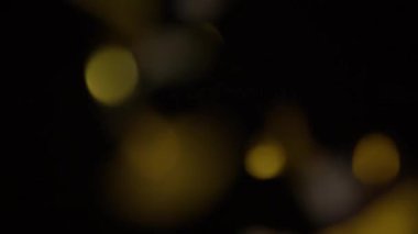 Blurry close-up shot of gold and silver confetti falling against a black background