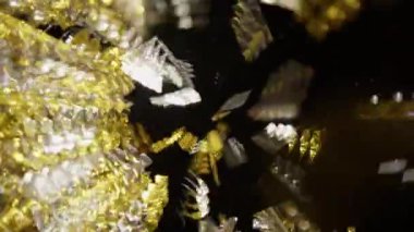 Gold and silver confetti are blown with video effects on a black background