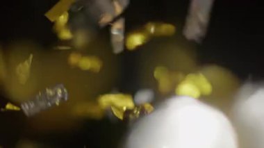 Close-up shot of a shower of shiny gold and silver confetti against a black background