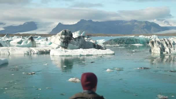 アイスランドのヨークサルロン氷河ラグーンを見て 男の後ろの景色を示す 上方に移動する昼間の広い傾きのショット — ストック動画