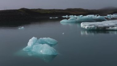 İzlanda 'daki Jokulsarlon Buzul Gölü' nün yüzen buzdağlarına odaklanarak soldan sağa hareket eden bir çekim.