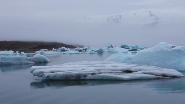 アイスランドのジョクルサロン氷河ラグーンの浮遊氷山と穏やかな水に焦点を当てて左から右に移動するパンショット — ストック動画