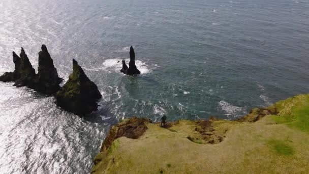 アイスランドのレイニストランガー岩の形成と海を見て崖の上に立っている男の昼間の空中ショット — ストック動画