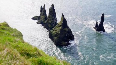 An aerial view showing the Reynisdrangar sea stacks with birds flying around, as waves hit the rocks located in Iceland