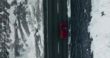 A top view shot of a lone red car traveling on a road during winter in Iceland