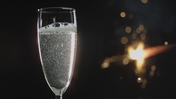 シャンパンで満たされたフルートガラスのクローズアップショット暗い背景を背景にぼんやりとした明るい輝きの後ろ — ストック動画