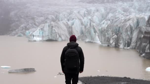 アイスランドのSkaftafellにある茶色の湖でSvinafellsjokull氷河を探している男の昼間のバックビューショット — ストック動画