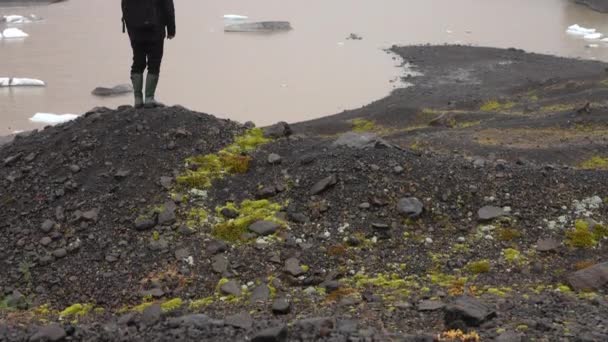 傾きは アイスランドのSkaftafellで昼間に霧のような雰囲気のあるSvinafellsjokull氷河を見ている岩の多い湖畔と男を示す上に移動しました — ストック動画