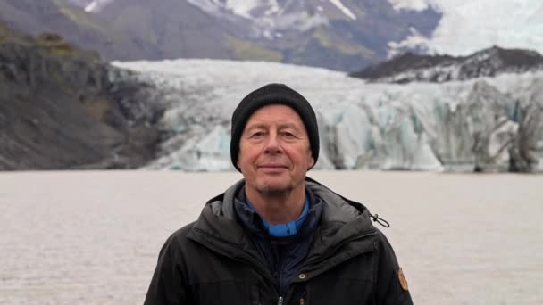 カメラをまっすぐに見て笑っている男の中近接ショット アイスランドのSkaftafellで昼間の背景にぼやけたSvinafellsjokull氷河と山脈 — ストック動画