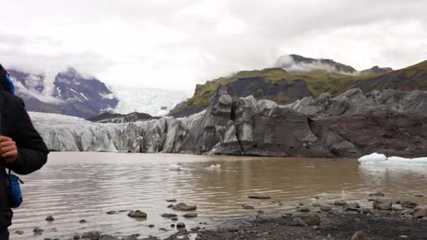 パンショットは右から左に移動美しいSvinafellsjokull氷河 そしてアイスランドのSkaftellで昼間にそれに対して立っている男を示しています — ストック動画