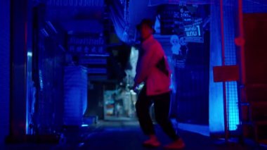 Modern sokak dansı yapan bir adam mavi ışıklı bir sokakta ağır çekimde hareket eder.