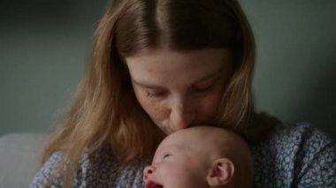 Bir anne, kollarında sarılırken esneyen bebeğinin başını öper.