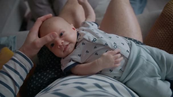 彼の額が優しく触れられている間 彼の父の膝の上に笑みを浮かべて新生児のトップビューショット — ストック動画