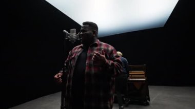 Adamın biri mikrofona şarkı söylerken, diğeri de piyanonun arkasından ona eşlik ederken.