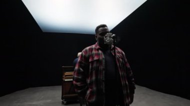 Bir adam mikrofona şarkı söylerken, diğeri de arkasında siyah arka planı ve beyaz ışıkları olan bir stüdyoda piyano çalıyor.