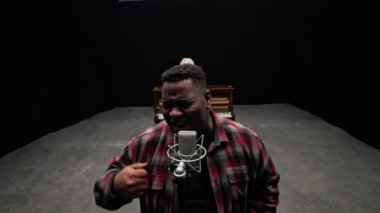 Ekose gömlekli bir adamın, arkasında bir piyanistle mikrofona şarkı söylerken el hareketi yaptığı en iyi görüntü.