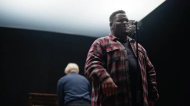 Bir piyanist arkasından çalarken parmaklarıyla mikrofona şarkı söylerken orta ölçekli bir görüntü.